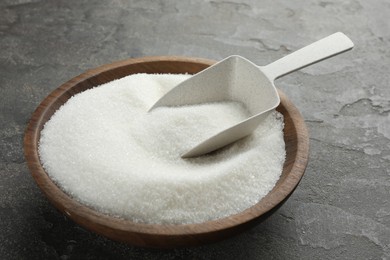 Photo of Granulated sugar in bowl and scoop on grey textured table, closeup