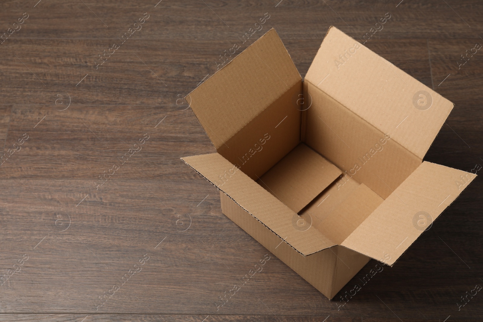 Photo of Empty open cardboard box on wooden table. Space for text