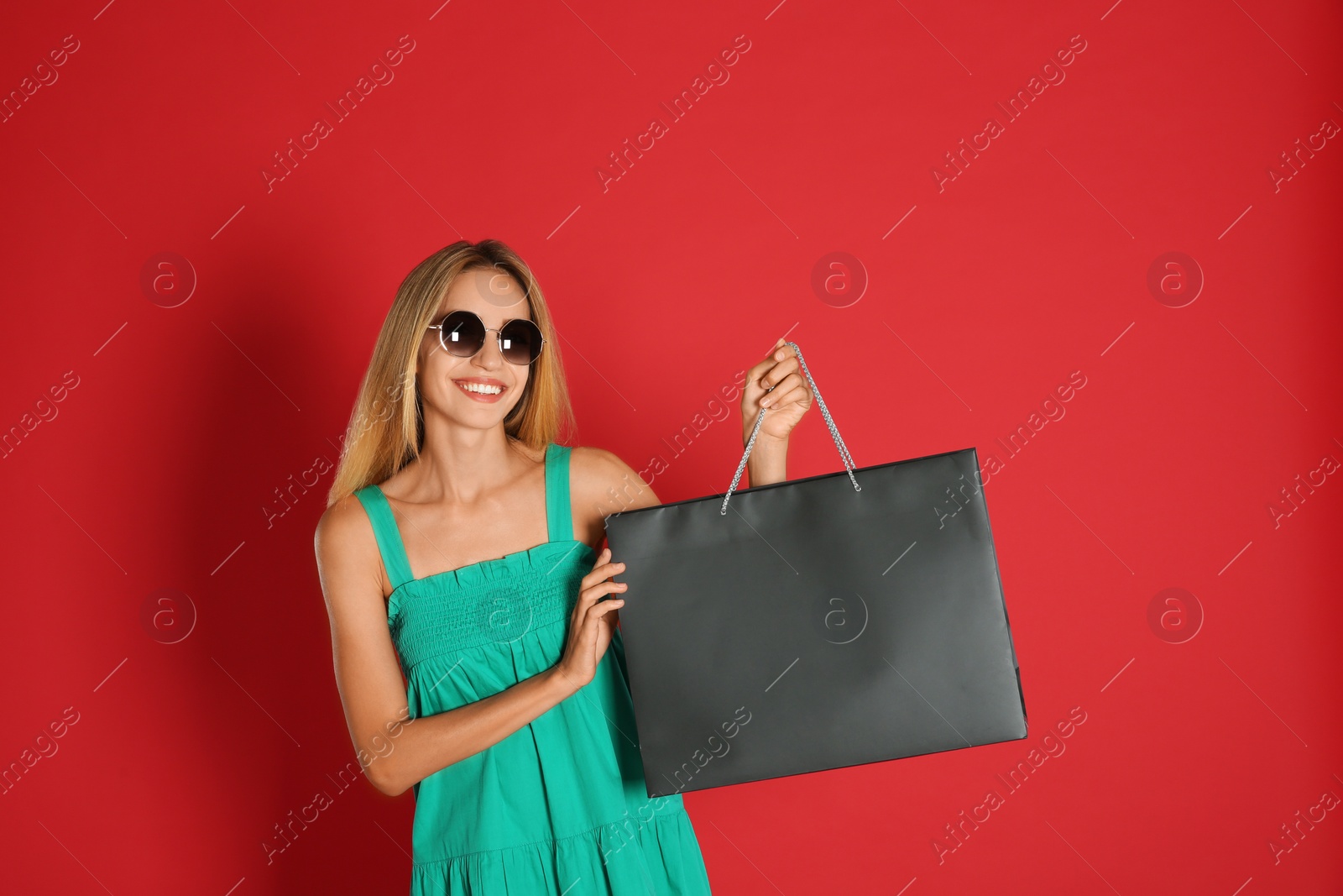 Photo of Happy young woman with shopping bag on red background. Black Friday Sale