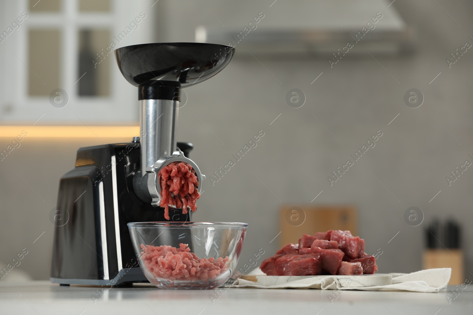 Photo of Electric meat grinder with beef mince on white table in kitchen