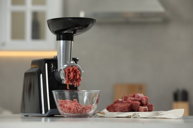 Photo of Electric meat grinder with beef mince on white table in kitchen