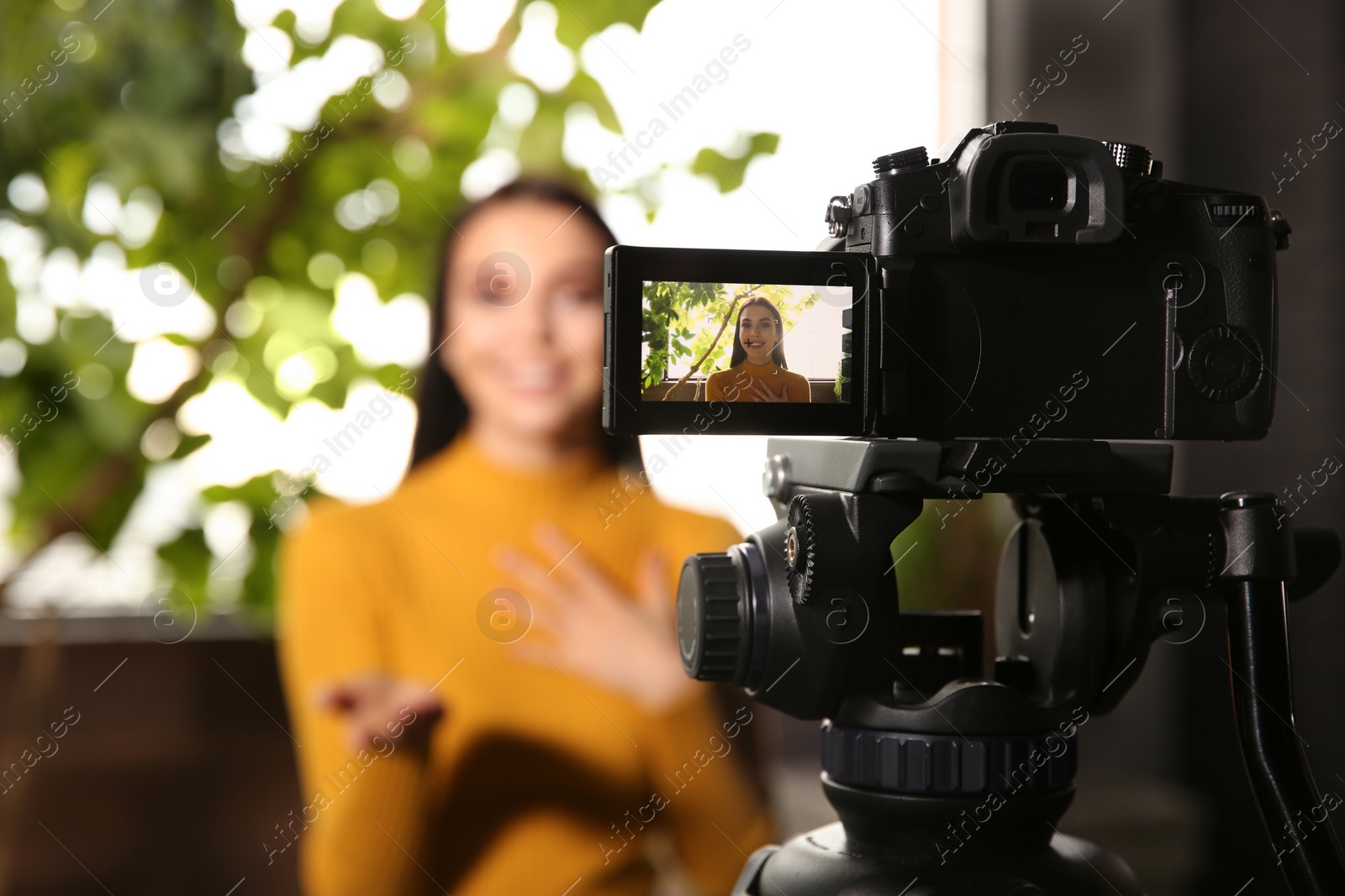 Photo of Young blogger recording video indoors, focus on camera screen