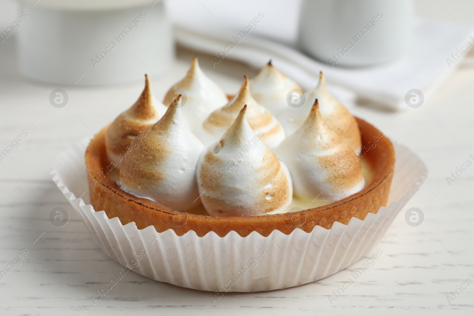 Photo of Tartlet with meringue on white wooden table, closeup. Delicious dessert