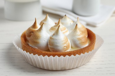 Tartlet with meringue on white wooden table, closeup. Delicious dessert