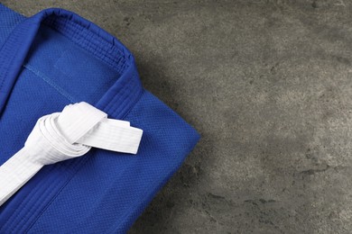 Photo of White karate belt and blue kimono on gray textured background, top view. Space for text