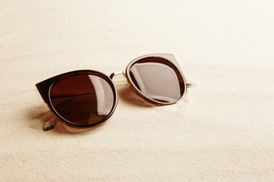 Stylish sunglasses on white sand, space for text. Summer time