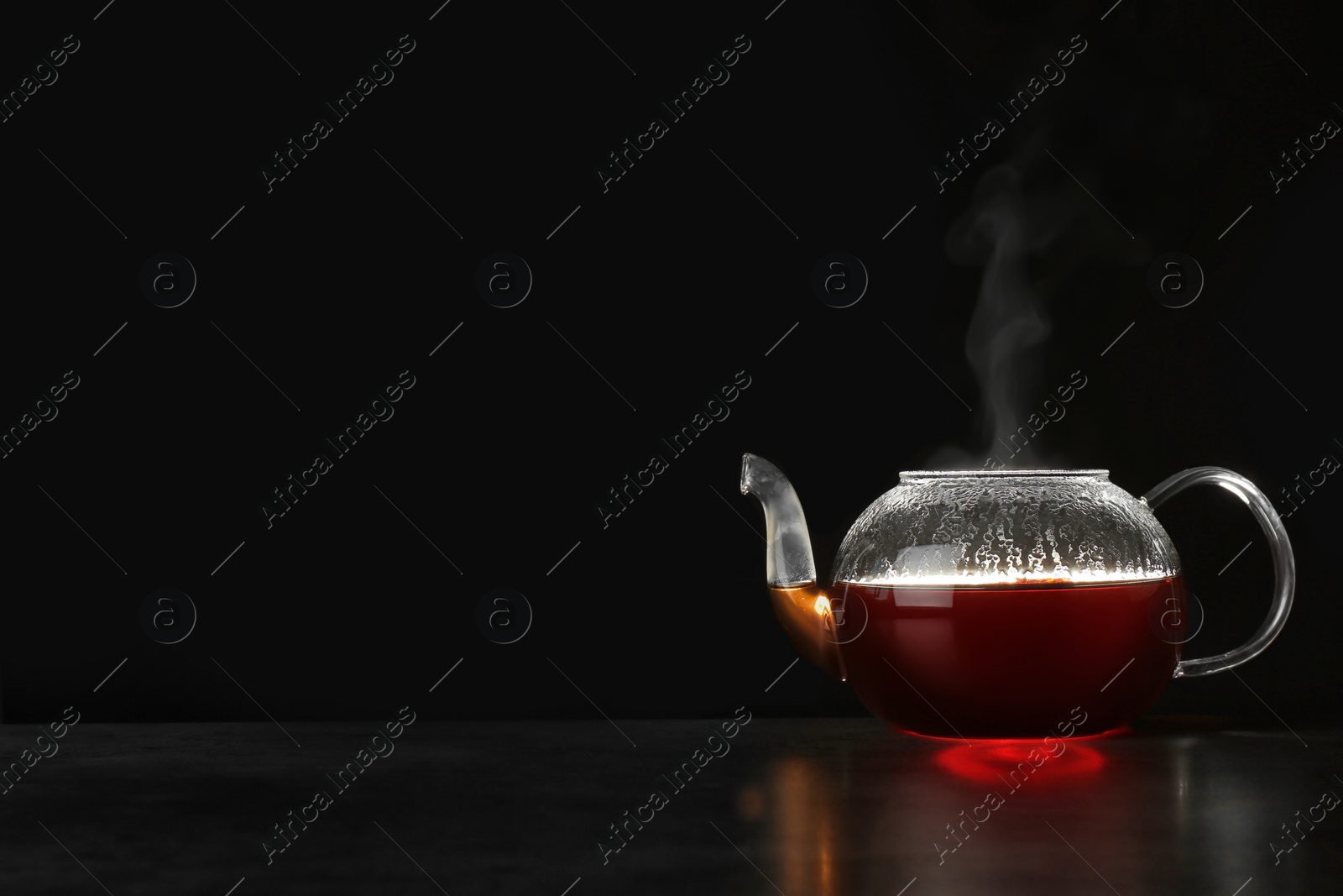 Photo of Glass teapot with delicious hot beverage on table against dark background. Space for text