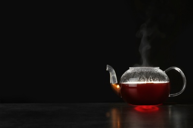 Photo of Glass teapot with delicious hot beverage on table against dark background. Space for text