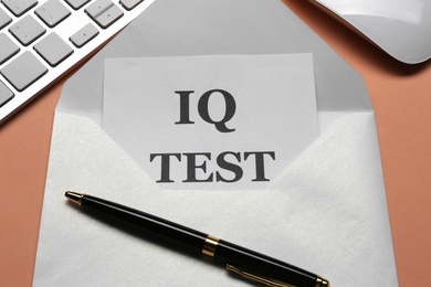 Note with text IQ Test in envelope, keyboard and mouse on coral background, closeup