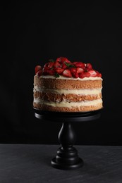 Photo of Tasty cake with fresh strawberries and mint on dark gray table against black background