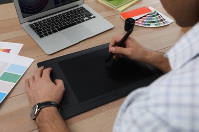 Professional designer with graphic tablet at wooden table, closeup