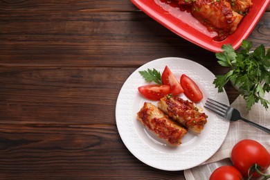 Photo of Delicious stuffed cabbage rolls with tomatoes served on wooden table, flat lay. Space for text