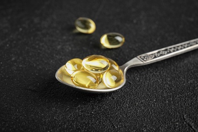 Photo of Spoon with cod liver oil pills on table, closeup