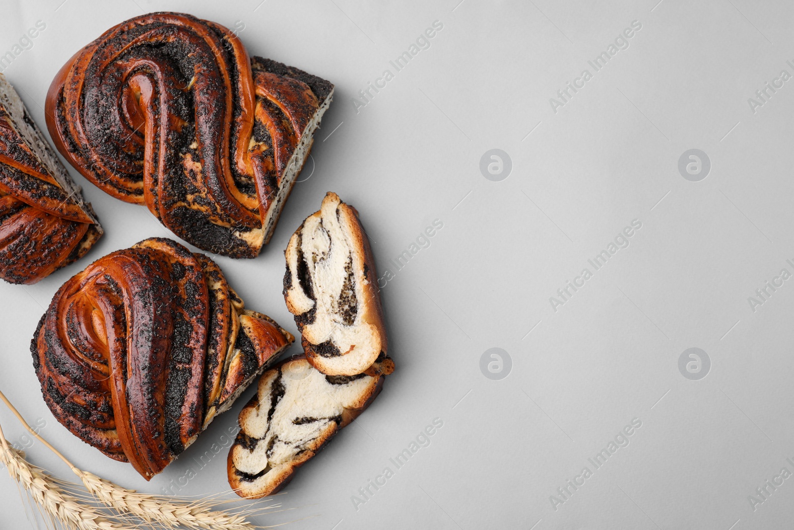 Photo of Pieces of poppy seed roll and spikelets on light grey background, flat lay with space for text. Tasty cake