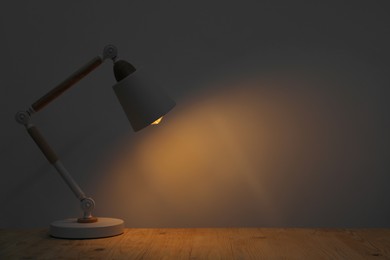 Photo of Stylish modern desk lamp on wooden table at night, space for text