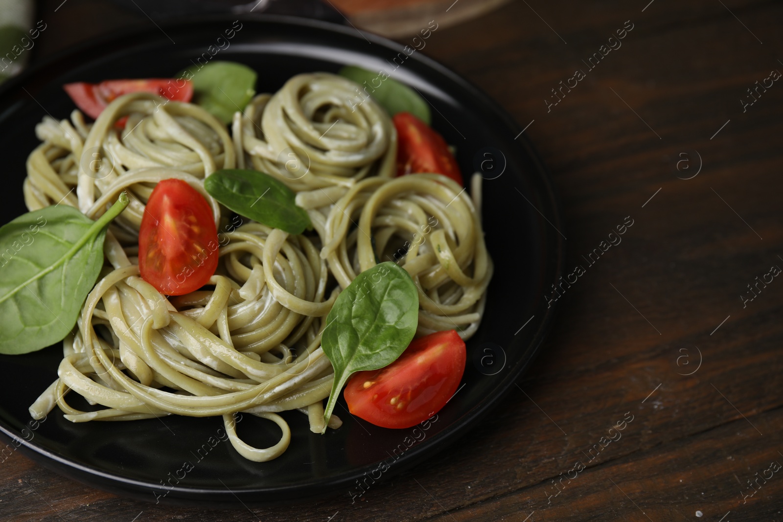 Photo of Tasty pasta with spinach, sauce and tomatoes on wooden table, space for text