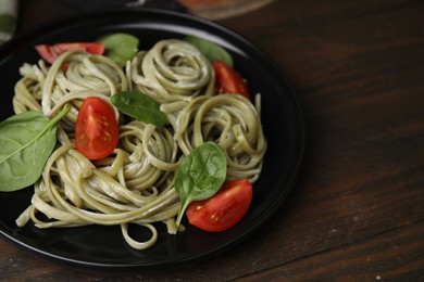 Photo of Tasty pasta with spinach, sauce and tomatoes on wooden table, space for text