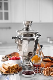 Photo of Traditional Russian samovar and treats on white table in kitchen