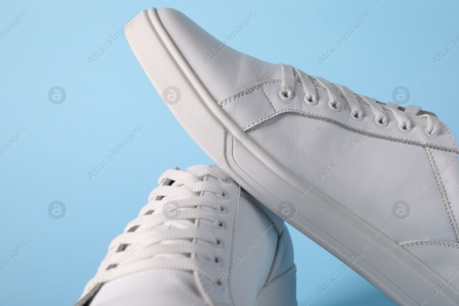 Photo of Pair of stylish white sneakers on light blue background, closeup