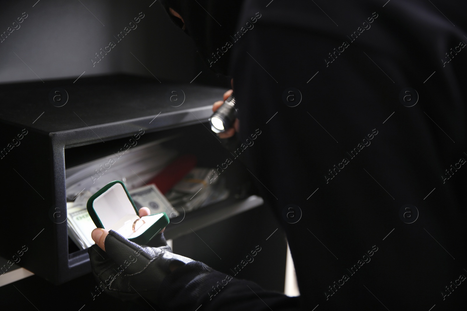 Photo of Thief taking golden ring out of steel safe indoors, closeup