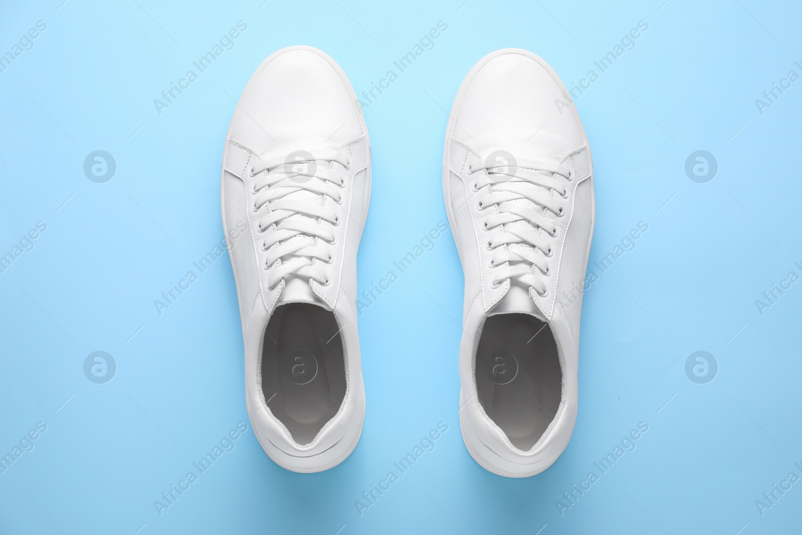 Photo of Pair of stylish white sneakers on light blue background, top view