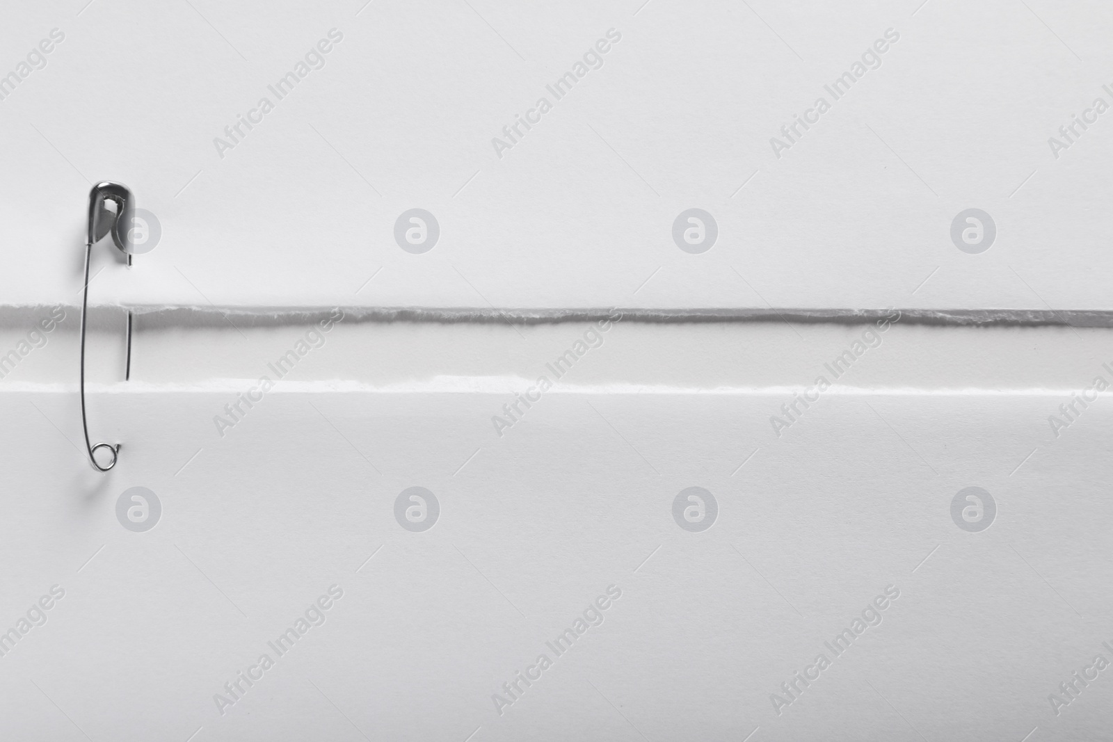 Photo of Pieces of paper sheets joined with safety pin on white background, top view