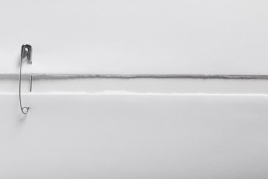 Photo of Pieces of paper sheets joined with safety pin on white background, top view