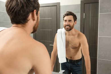Photo of Handsome bearded man looking at mirror in bathroom near wooden doors