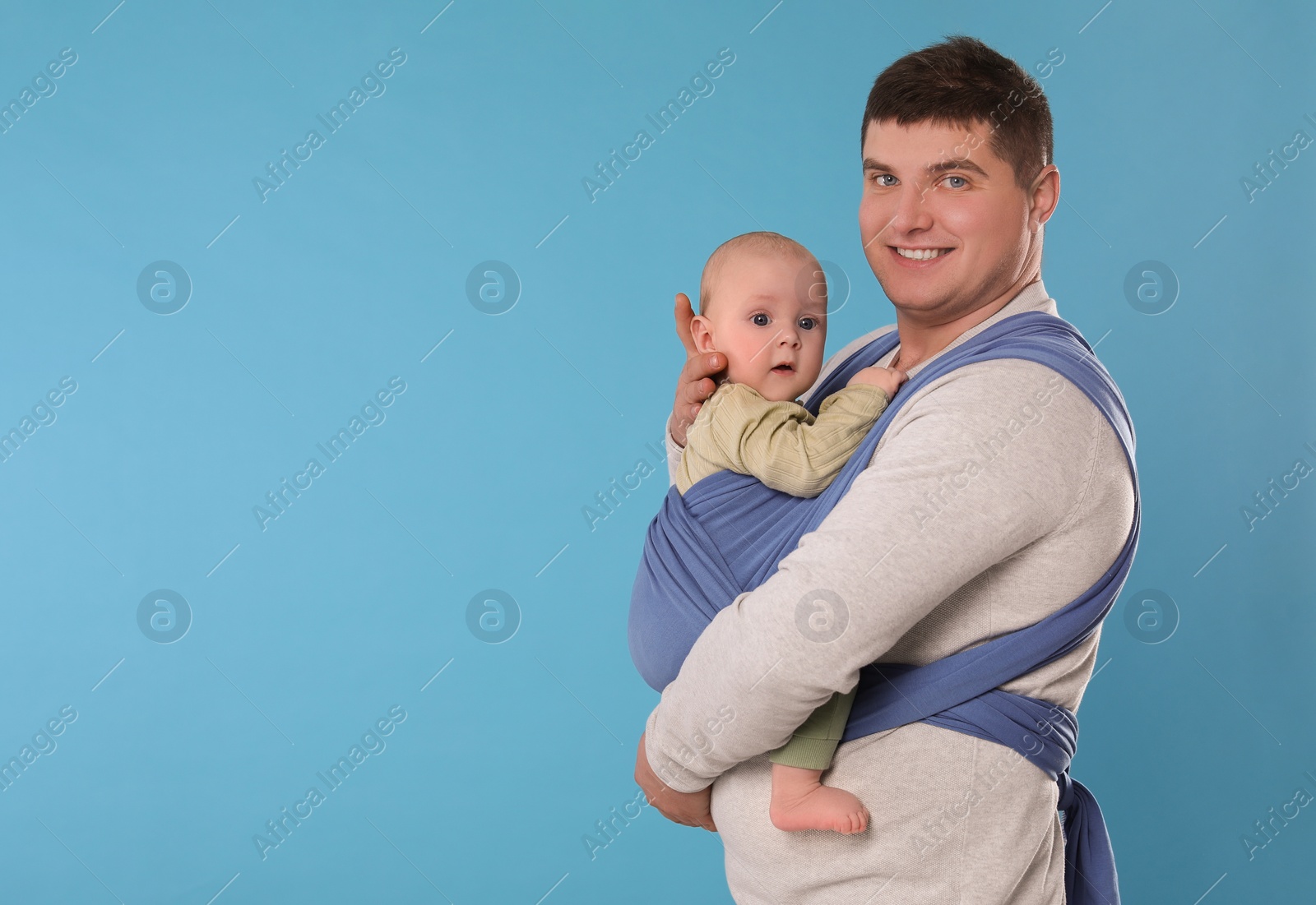 Photo of Father holding his child in sling (baby carrier) on light blue background. Space for text