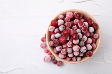 Photo of Frozen red cranberries in bowl on white table, top view. Space for text