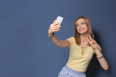 Attractive young woman taking selfie on color background