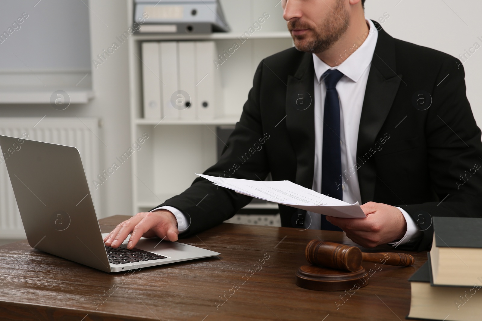 Photo of Law and justice. Lawyer working with documents and laptop at wooden table in office, closeup