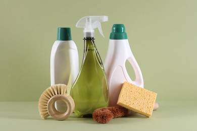 Bottles of cleaning product, brushes and sponge on light green background