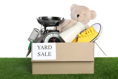 Photo of Sign Yard Sale written on box with different stuff on green grass against white background