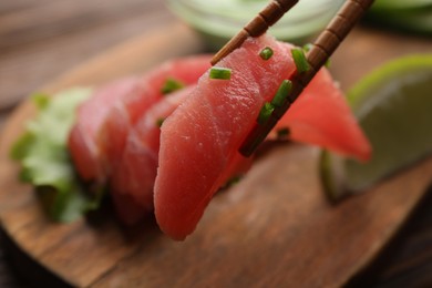 Photo of Holding tasty sashimi (piece of fresh raw tuna) with chopsticks against blurred background, closeup