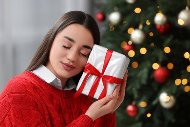 Photo of Beautiful woman with gift box near Christmas tree indoors