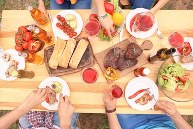 Photo of Young people having barbecue at table outdoors, top view