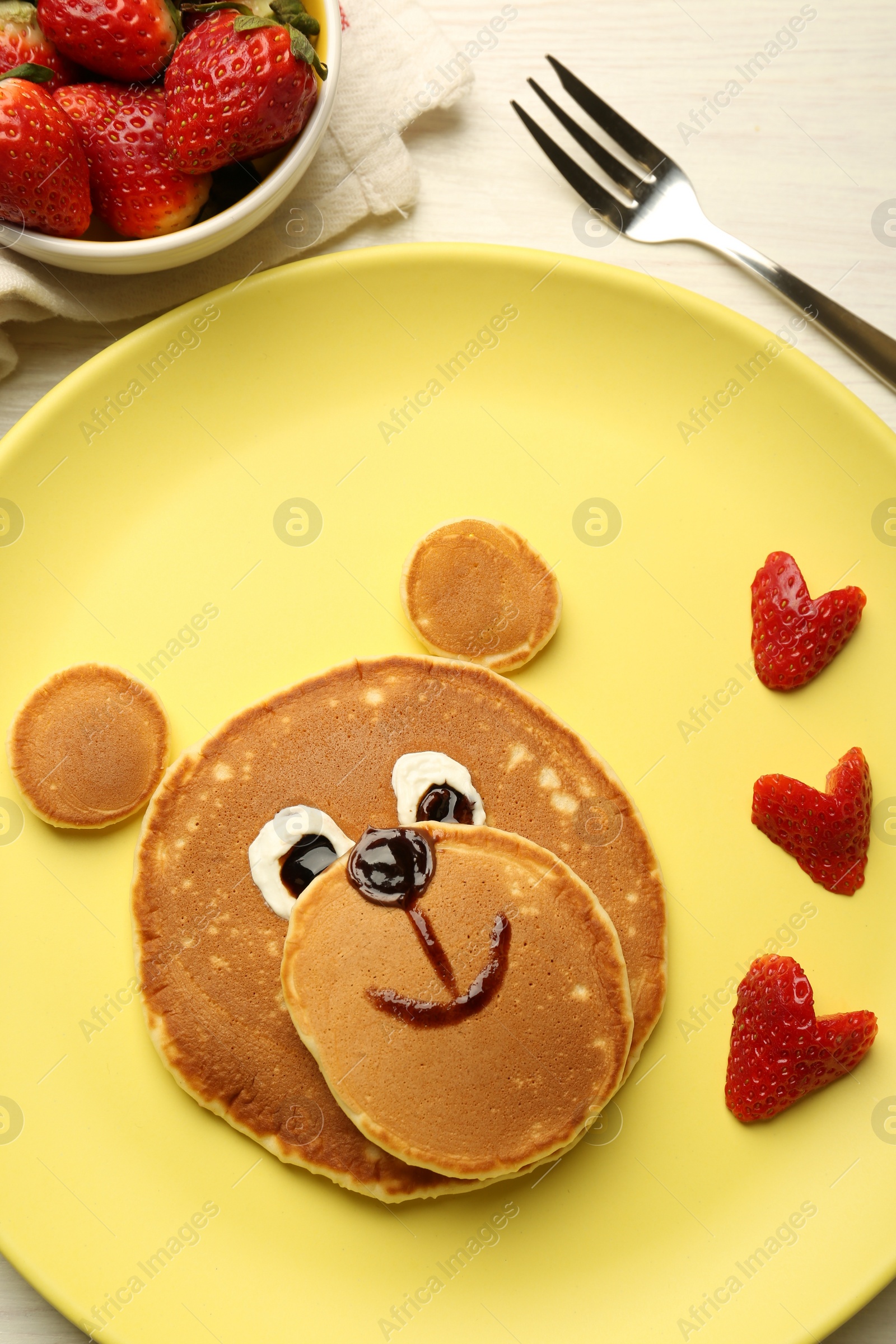 Photo of Creative serving for kids. Plate with strawberries, cute bear made of pancakes on light wooden table, flat lay