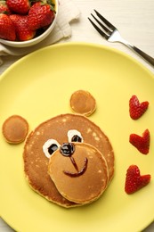 Creative serving for kids. Plate with strawberries, cute bear made of pancakes on light wooden table, flat lay