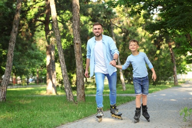 Father and son roller skating in summer park