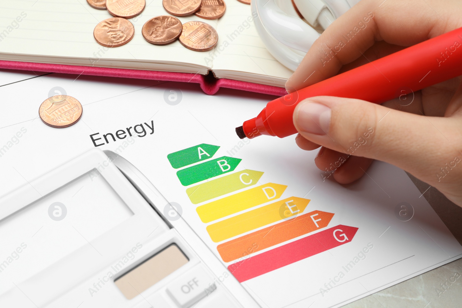 Photo of Woman with marker, energy efficiency rating chart and calculator at table, closeup