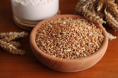 Photo of Wheat grains in bowl, flour and spikes on wooden table