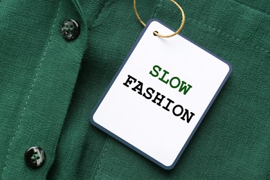 Image of Conscious consumption. Tag with words Slow Fashion on green shirt, top view