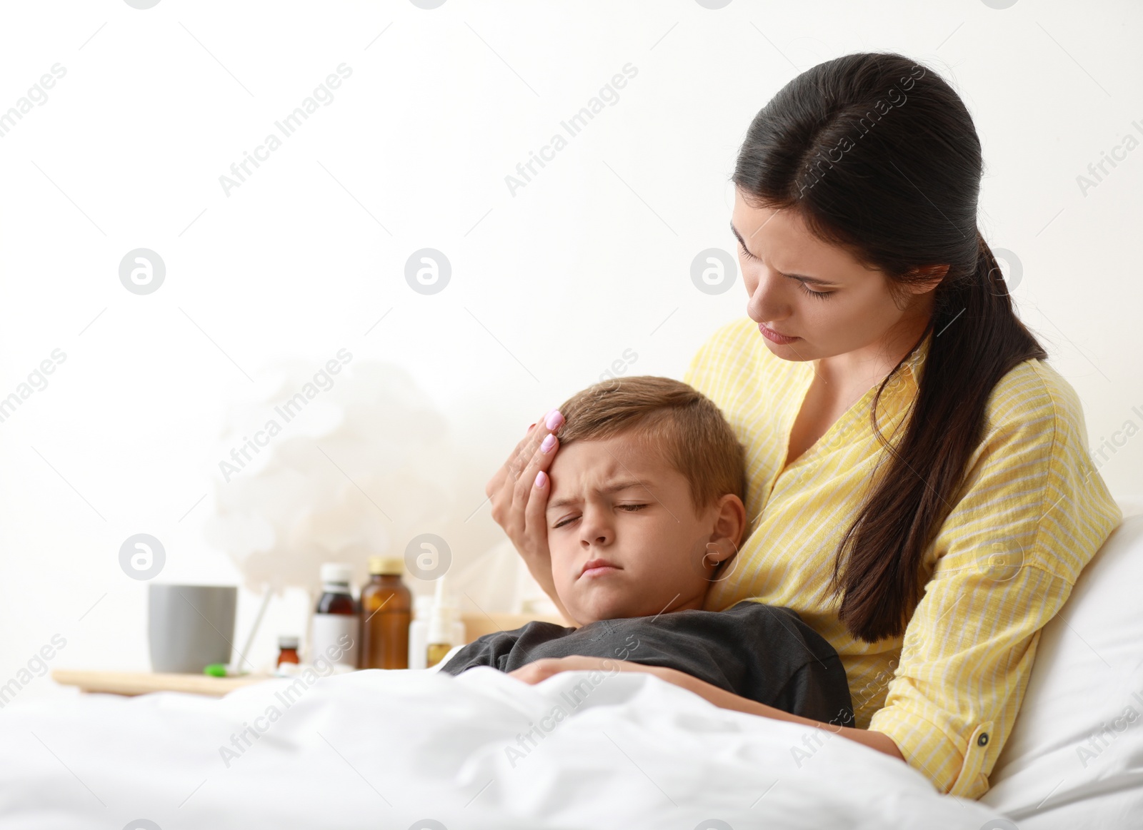 Photo of Mother taking care of her little son suffering from cold in bed