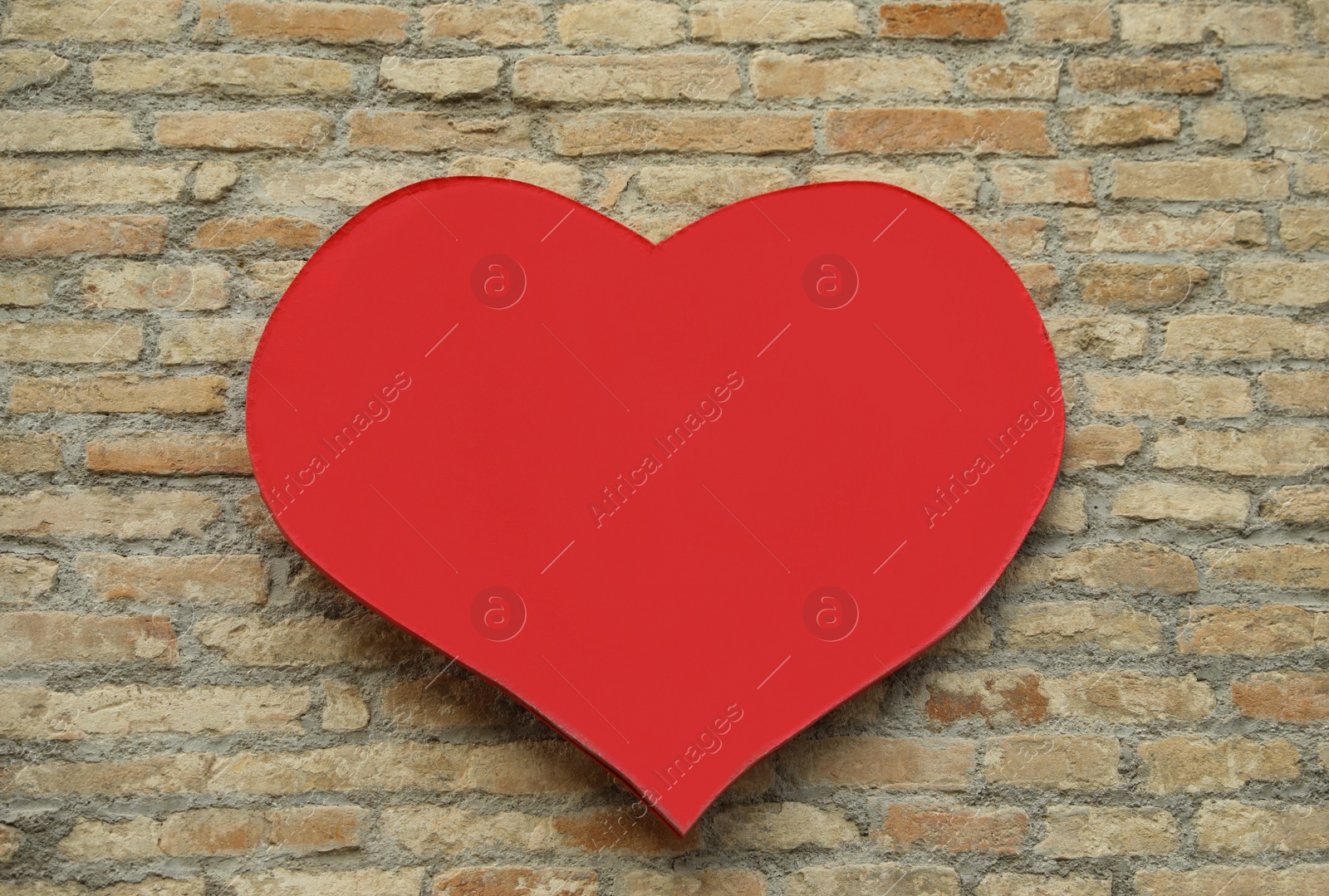 Photo of Empty heart shaped sign on brick wall. Space for design