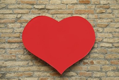 Photo of Empty heart shaped sign on brick wall. Space for design