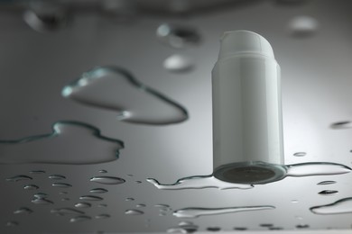 Photo of Moisturizing cream in bottle on glass with water drops against grey background, low angle view. Space for text