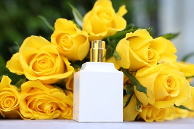 Perfume and beautiful bouquet of yellow roses on light table, closeup