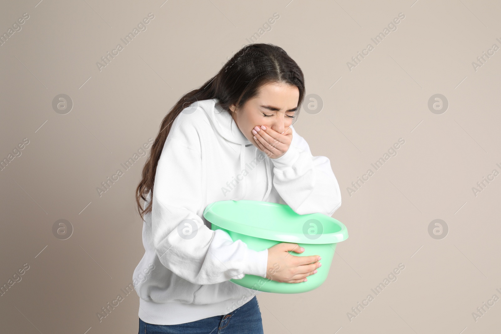 Photo of Young woman with basin suffering from nausea on beige background. Food poisoning