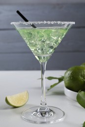 Photo of Delicious Margarita cocktail with ice cubes in glass and lime on white table